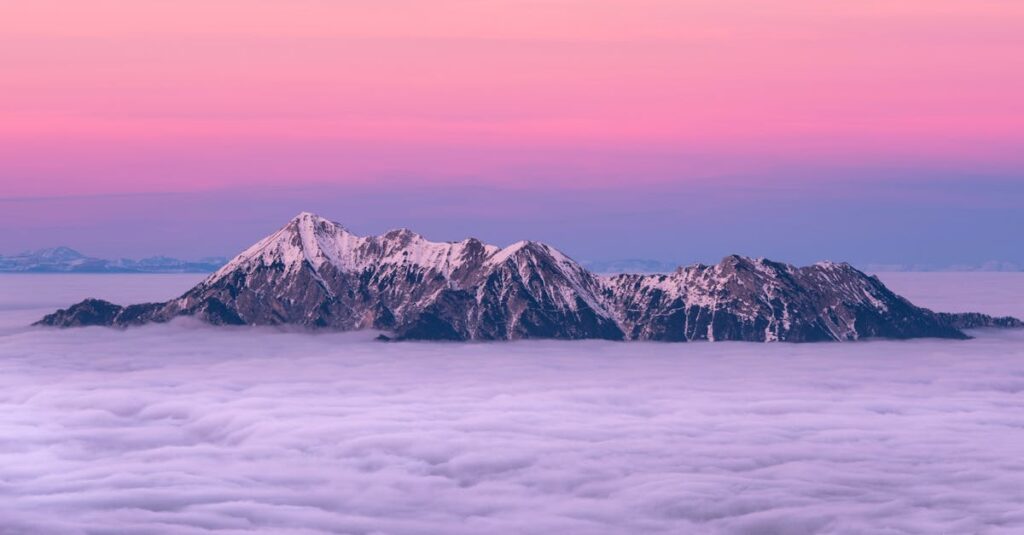 Breathtaking view of a snow-covered mountain peak rising above clouds during a stunning pink sunrise.